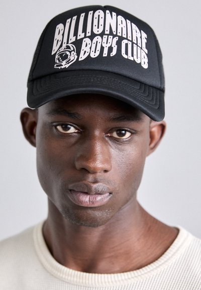 Schwarze Baseballmütze mit dem "Billionaire Boys Club"-Logo in weißem Text und Astronauten-Grafik. Getragen mit einem hellen, strukturierten Pullover.