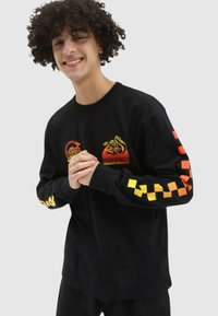 Svart långärmad T-shirt med grafiska mönster i röd, orange och gul. Har rutiga mönster på ärmarna och broderade detaljer.