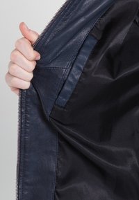 Mörkblå läderjacka med dragkedja, som visar en slät utsida och ett svart texturerat foder. Detaljerad sömnad längs sömmarna.