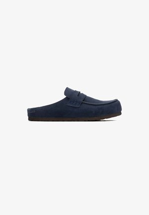 Zapato mule azul marino sin cordones con parte superior de ante y suela de goma marrón, visto desde un lado sobre un fondo blanco.