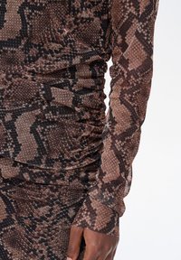 Brązowa i czarna tkanina w wzór skóry węża o fakturowanej powierzchni z marszczonymi detalami; długie rękawy z dopasowanymi mankietami.