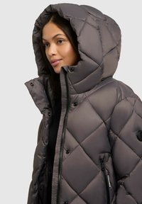 Veste en duvet grise avec une grande capuche, motif matelassé en losanges, fermeture éclair noire et boutons-pression. Elle dispose de poches latérales et d'un patch logo.