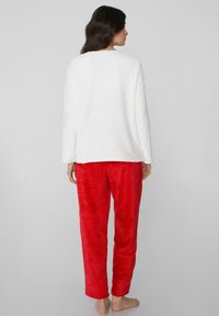 Biały polarowy top z długim rękawem połączony z miękkimi czerwonymi spodniami o fakturze. Prosty fason, luźne dopasowanie i odkryte plecy. Brak wzorów i widocznych elementów metalowych.