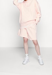 Sudadera rosa claro con cordón, diseño en capas y pantalones cortos rosas a juego. Combinado con zapatillas blancas y calcetines hasta el tobillo. Tejido de mezcla de algodón.