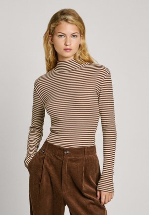 Jersey de cuello alto a rayas marrón y crema con mangas largas, diseño ajustado, hecho de material acanalado. Llevado con pantalones de pana marrones.