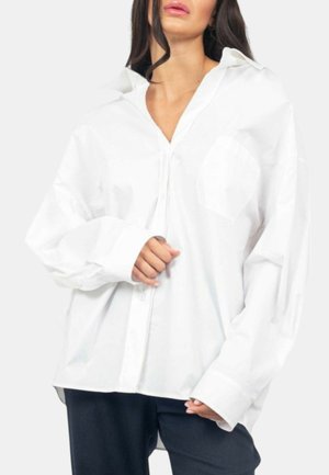Camicia bianca oversize con bottoni, dotata di colletto, due tasche sul petto e maniche lunghe. Realizzata in tessuto liscio, presenta un orlo dritto.