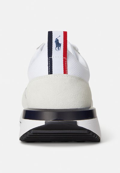Fehér sportcipő texturált velúr sarokkal, tengerészkék és piros csíkos húzófüllel, valamint fényes fekete talppal. Klasszikus logó részlet a fülön.