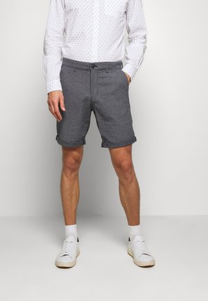 Grå linnedshorts med rullekanter, parret med en hvid skjorte med blå prikker. Hvide sneakers fuldender outfittet.