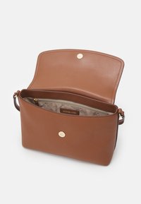 Sac à main en cuir marron avec rabat ouvert montrant la doublure intérieure beige et une poche zippée avec étiquette Michael Kors à l'intérieur.