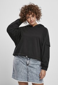 Sudadera negra ligera con un ajuste relajado y dobladillo con cordón, combinada con una falda de mezclilla azul claro con cierre de botones en el frente y dobladillo deshilachado.