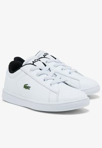 White sneakers with a smooth leather texture, featuring black laces and a green embroidered crocodile logo on the side. Rounded toe design.