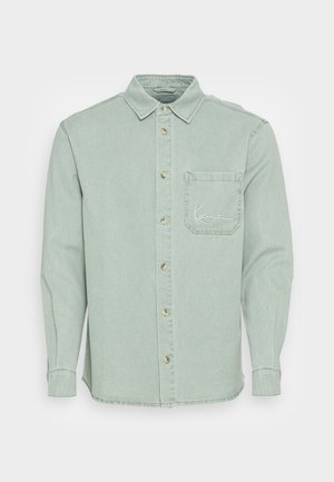 Lysegrøn langærmet skjorte med knapper, brystlomme og diskret hvid logo-broderi på lommen.