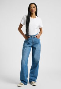Camiseta de algodón blanca ligera combinada con vaqueros de denim azul de cintura alta y corte holgado. Los vaqueros tienen un diseño clásico y costuras visibles.