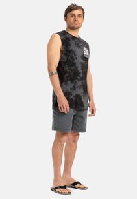 Black tie-dye sleeveless shirt with white graphic on chest, paired with gray shorts and black flip-flops, standing on a white background.