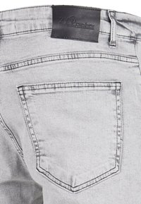 Jeans en denim gris avec une étiquette en cuir noir à la taille, dotés de poches arrière plates et de double couture le long des coutures.