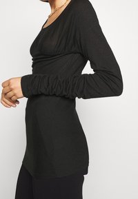 Zwart top met lange mouwen gemaakt van lichtgewicht, gestructureerde stof met een ronde halslijn en plooidetail langs het bovenlichaam. Slim fit.