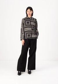 Long-sleeve button-up shirt with a black and beige geometric pattern; paired with wide-leg black pants and shiny black ankle boots.
