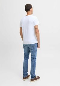 Bela majica s kratkimi rokavi, modri jeans, rjave čevlje. Majica ima okrogel ovratnik in ravno prileganje. Preprost, minimalističen dizajn.