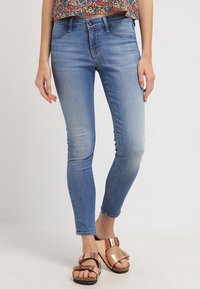 Tajta jeans i ljusblå denim, med medelhög midja, fem fickor och subtil blekning. Kombinerade med glänsande bronsfärgade sandaler.