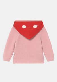 Pletený svetr se světlým růžovým tělem a červenou trojúhelníkovou kapucí se dvěma bílými tečkami, který se vyznačuje texturovaným a pohodlným designem a dlouhými rukávy.