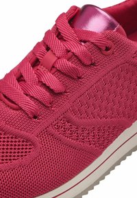 Baskets en maille rose avec tissu texturé, lacets plats, accent métallique sur le talon, et semelle intermédiaire blanche avec détail de rayure rouge.