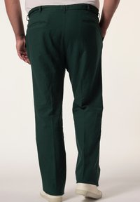 Pantaloni in cotone verde con una vestibilità rilassata, dotati di tasche laterali, vita con cordoncino e una texture liscia. Indossati con scarpe bianche.