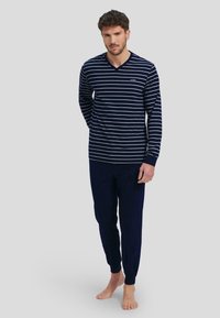 Blusa de manga larga en rayas navy y blanca con escote en V, combinada con pantalones navy de cintura elástica, ambos de una tela suave. Branding minimalista en el pecho.