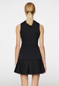 Black sleeveless top with a fitted design, paired with a pleated black skirt. Smooth fabric texture; simple, clean lines.