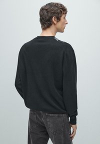 Schwarzer Pullover aus weichem Material mit Rundhalsausschnitt und langen Ärmeln, kombiniert mit dunkelgrauen Jeans. Schlichtes Design ohne Muster.