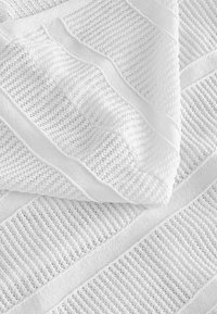 Tissu tricoté blanc avec des rayures alternées en maille serrée et ajourée créant un motif texturé et plié.