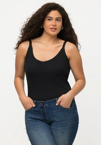 Canottiera nera a costine con scollatura a V, abbinata a jeans aderenti in denim di lavaggio medio, dotati di tasche e leggeri segni di usura.