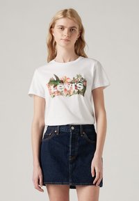 Camiseta blanca de algodón con un diseño floral colorido y el logo de "Levi's". Combinada con una falda de mezclilla oscura. Mangas cortas, cuello redondo.
