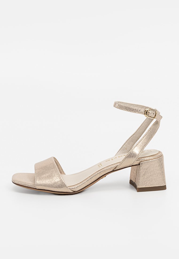 Sandal in oro metallico con punta quadrata aperta, sottile cinturino alla caviglia e tacco corto e spesso. Texture liscia con design minimalista.