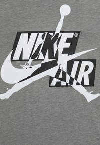 Szary bawełniany T-shirt z dużym czarno-białym logo Nike Air, z grafiką skaczącej postaci na środku.