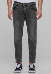 Pantalones de mezclilla gris oscuro con un corte ajustado, diseño de cinco bolsillos y detalles de costura visibles. Combinados con zapatillas negras y blancas.