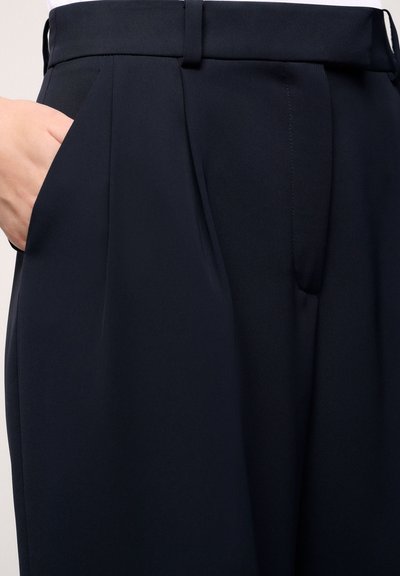 Mornarske krojene hlače s glatkim materijalom, plisama i bočnim džepom, s elegantnim pojasom i sjajnom završnom obradom.