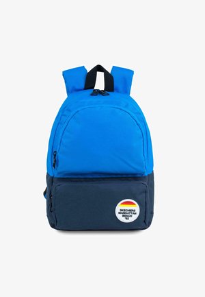 Mochila azul con un bolsillo frontal con cremallera, tirantes negros y un parche de logo con rayas rojas, amarillas y naranjas. El material parece duradero.