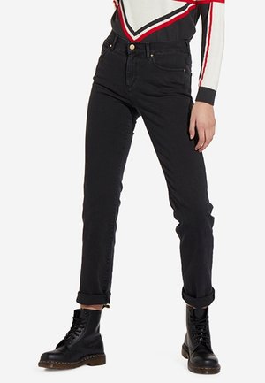 Osoba nosząca czarne wąskie dżinsy podwinięte przy kostkach, czarne botki sznurowane i białą bluzkę z długim rękawem w czerwone i czarne paski.