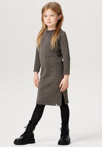 Graues Langarmkleid mit texturierter Oberfläche, Seitenschlitz, kombiniert mit schwarzen Schnürstiefeln und schwarzen Strumpfhosen mit goldenen Sternen.