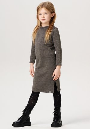 Graues Langarmkleid mit texturierter Oberfläche, Seitenschlitz, kombiniert mit schwarzen Schnürstiefeln und schwarzen Strumpfhosen mit goldenen Sternen.