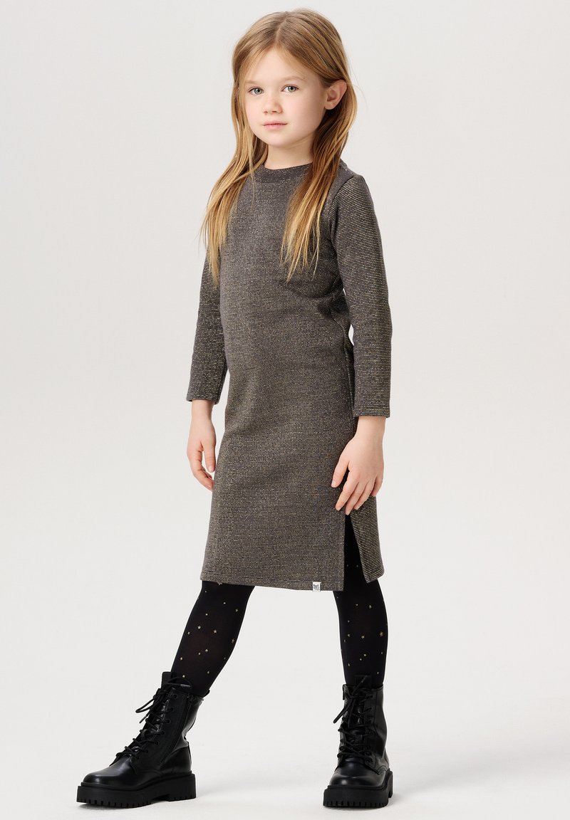 Graues Langarmkleid mit texturierter Oberfläche, Seitenschlitz, kombiniert mit schwarzen Schnürstiefeln und schwarzen Strumpfhosen mit goldenen Sternen.