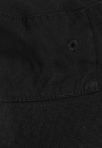 Svart bucket hat i texturerat material, med en strukturerad skärm, sydda detaljer och ett cirkulärt ventilationshål på toppen.