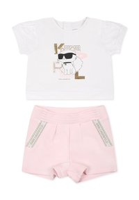 T-shirt blanc à manches courtes avec un graphisme de chat et des accents dorés, associé à un short rose texturé avec une large taille et des détails de logo.