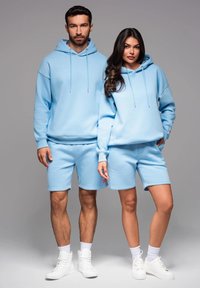 Des sweats à capuche bleu clair et des shorts en tissu doux, dotés de cordons de serrage et de poignets côtelés. Les deux portent des baskets blanches. Design simple, sans motifs.