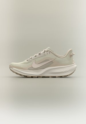 Jasnobeżowy but do biegania marki Nike z cholewką z siateczki, białą podeszwą, logo Swoosh po boku oraz wyściełanym kołnierzem dla wygody, pokazany z profilu.