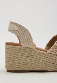 Sandalia de cuña beige con tacón de yute trenzado, tiras de tela texturizada y una amplia correa en el tobillo. Plantilla suave en marrón claro.