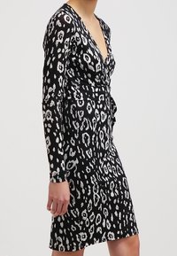 Svart klänning med djup V-ringning och långa ärmar, prydd med ett vitt leopardmönster, åtsittande vid midjan för struktur.