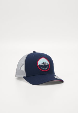 Boné azul marinho com parte traseira em rede, apresentando um emblema circular com montanhas e o nome da marca "Columbia Sportswear Co." Detalhes vermelhos em torno do emblema.