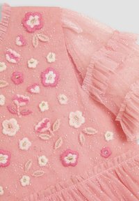 Robe en tulle rose ornée de broderies florales blanches et roses, avec une finition texturée et des paillettes dispersées. Détail de décolleté à volants.