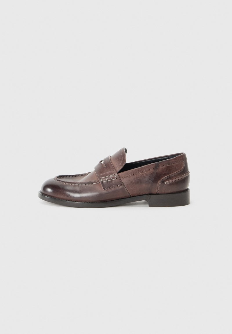 Brune lærloafers med en sydd design, rund tå og lav hæl. Har en hævet rem over vristen og dekorative detaljer.
